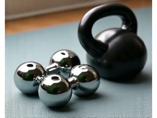 Ein Set aus unterschiedlichen Hanteln und Kettlebells auf einem sauberen Trainingsboden.